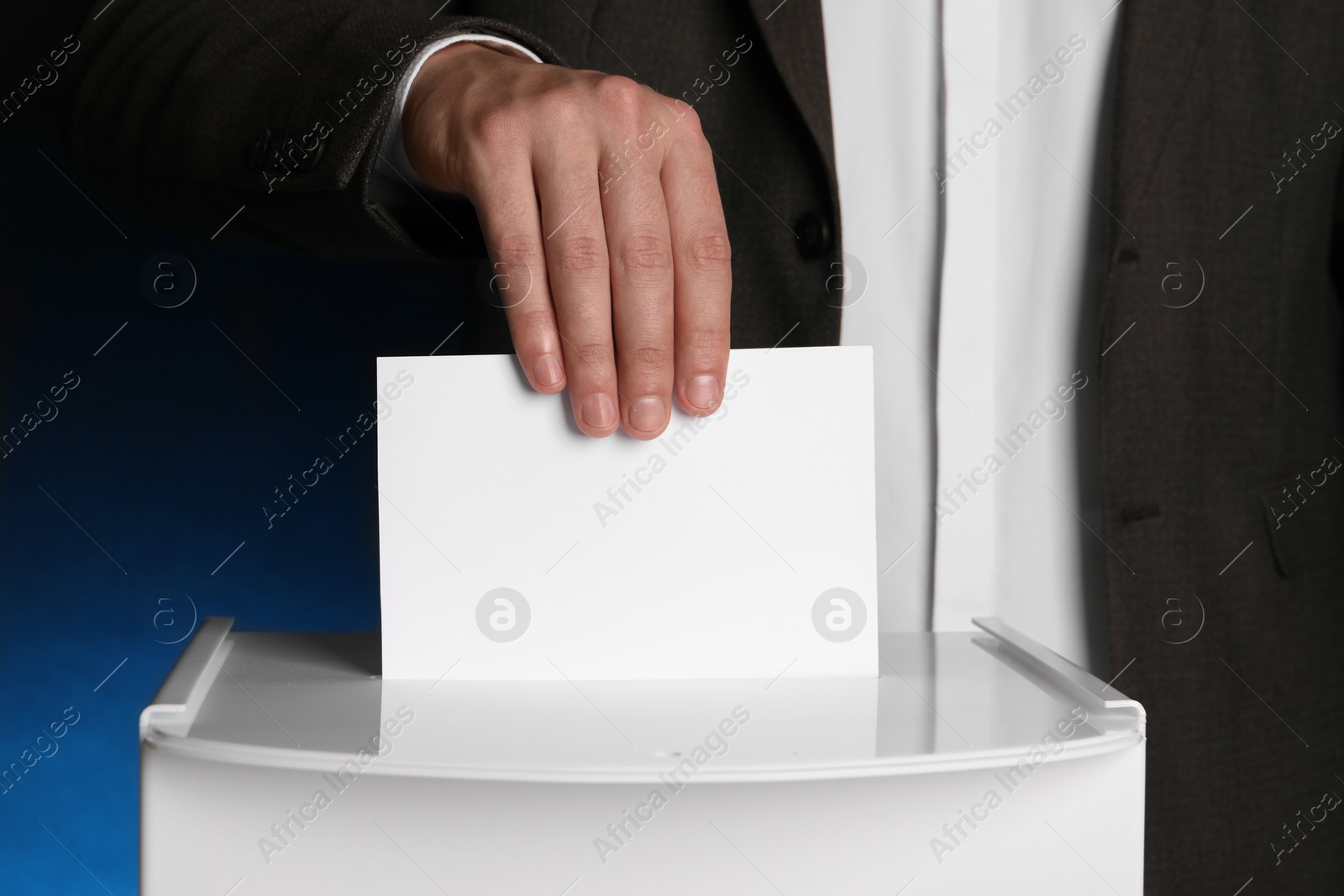 Photo of Man putting his vote into ballot box on dark blue background, closeup