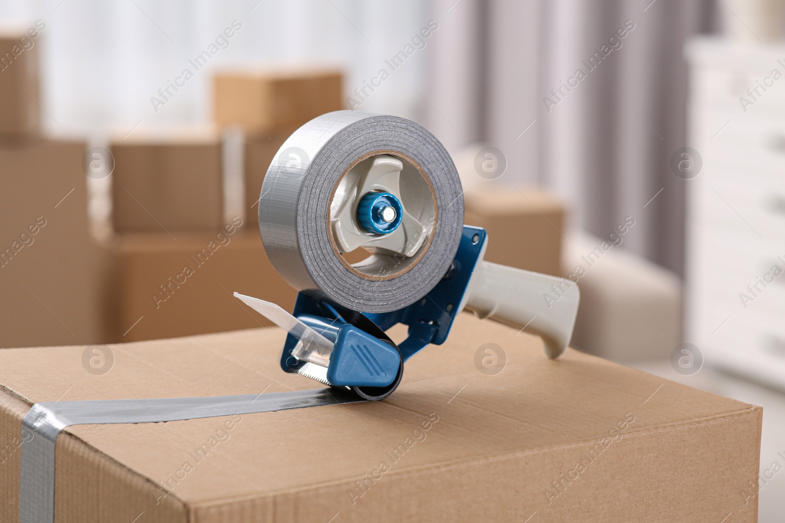 Photo of Dispenser with roll of adhesive tape on box indoors, closeup