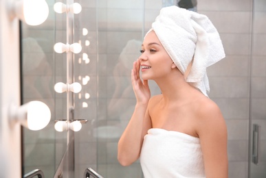 Photo of Beautiful woman with clean towels near mirror in bathroom