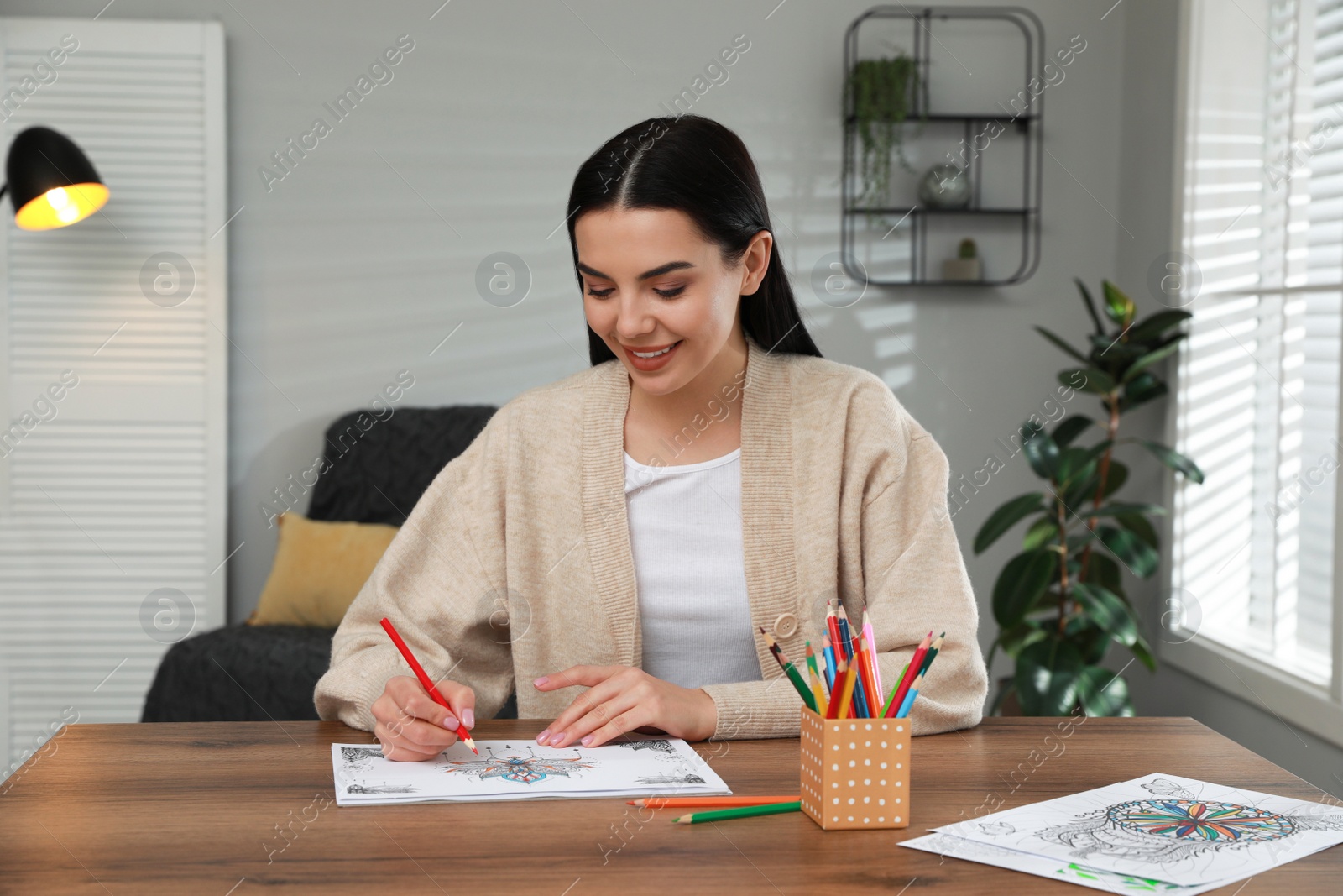 Photo of Young woman coloring antistress page at table indoors