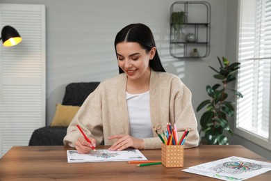 Photo of Young woman coloring antistress page at table indoors