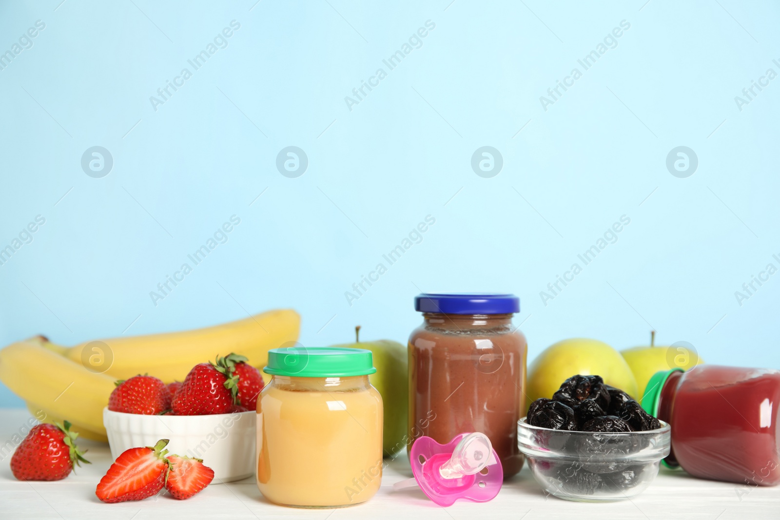 Photo of Jars with baby food and fresh ingredients on white wooden table against light blue background, space for text