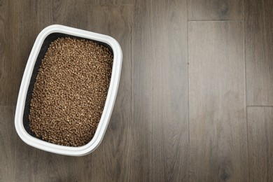 Photo of Cat litter tray with filler on wooden floor, top view. Space for text