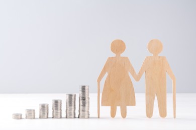 Pension savings. Figure of senior couple and stacked coins on white wooden table