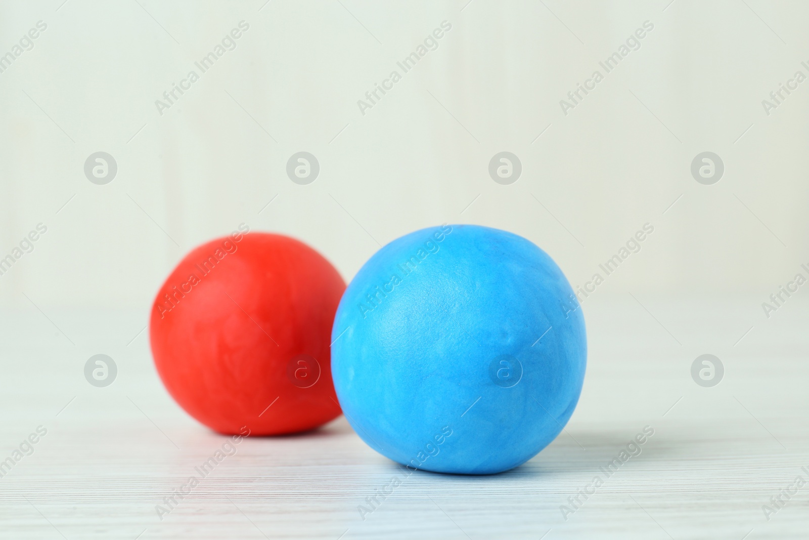 Photo of Different color play dough balls on white wooden table, closeup