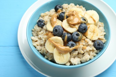Photo of Tasty oatmeal with banana, blueberries and peanut butter served in bowl on light blue wooden table, closeup