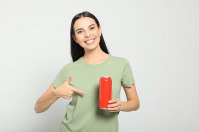 Beautiful happy woman holding red beverage can on light grey background