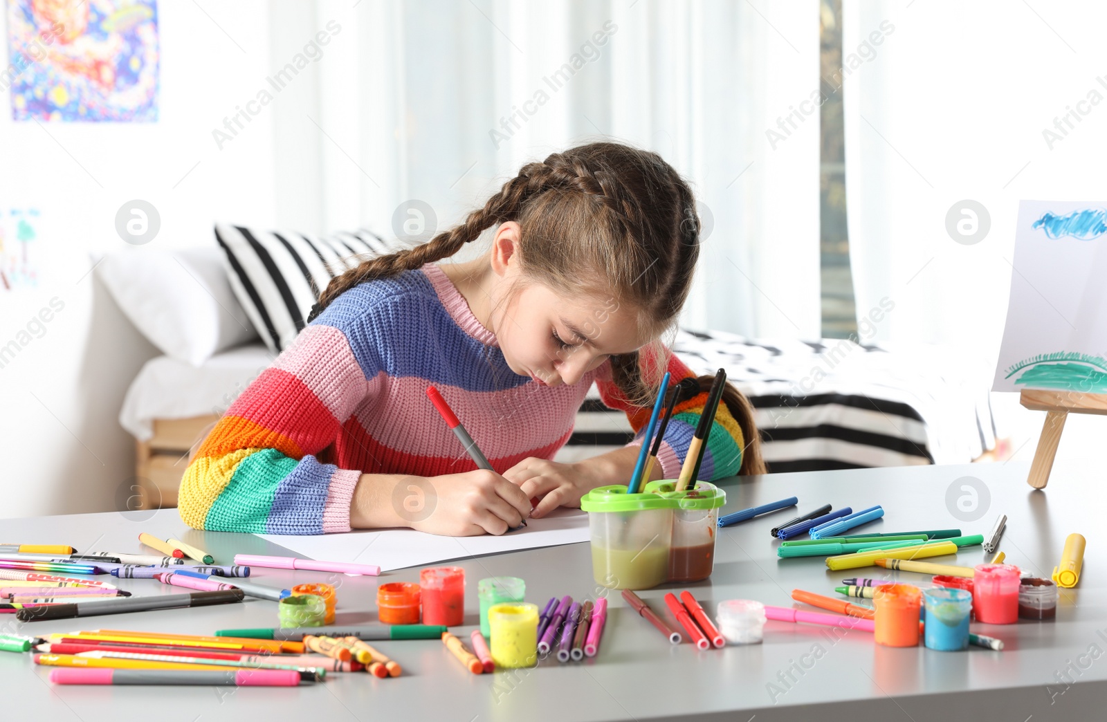 Photo of Little girl drawing picture at table with painting tools indoors