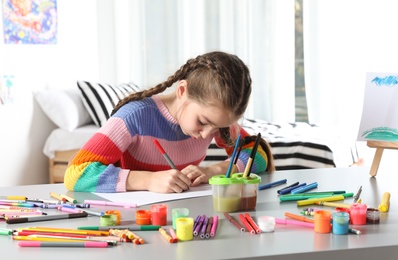 Photo of Little girl drawing picture at table with painting tools indoors