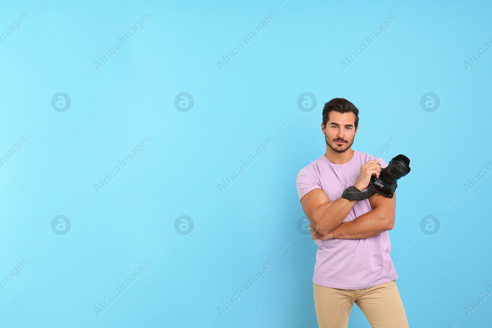 Photo of Young photographer with professional camera on light blue background. Space for text