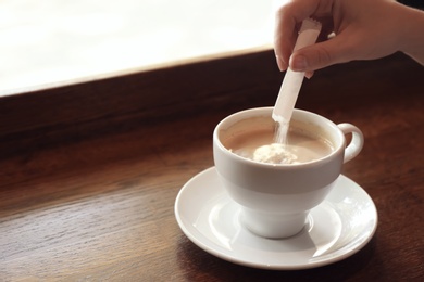 Photo of Woman adding sugar to fresh aromatic coffee on table, closeup