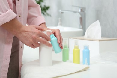 Woman pouring cosmetic product into plastic bottle at white countertop in bathroom, closeup. Bath accessories