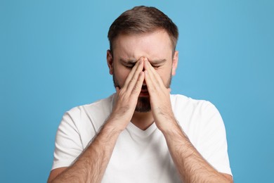 Photo of Young man suffering from headache on light blue background