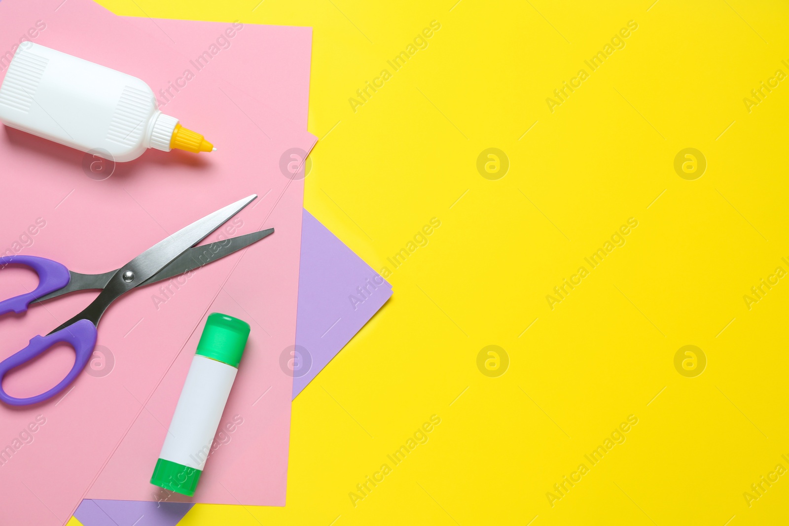 Photo of Glue, colorful paper and scissors on yellow background, flat lay. Space for text