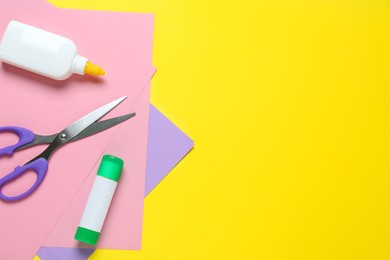 Glue, colorful paper and scissors on yellow background, flat lay. Space for text