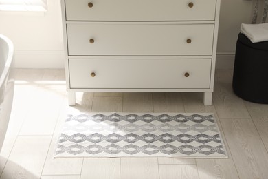 Stylish mat with pattern near chest of drawers in bathroom