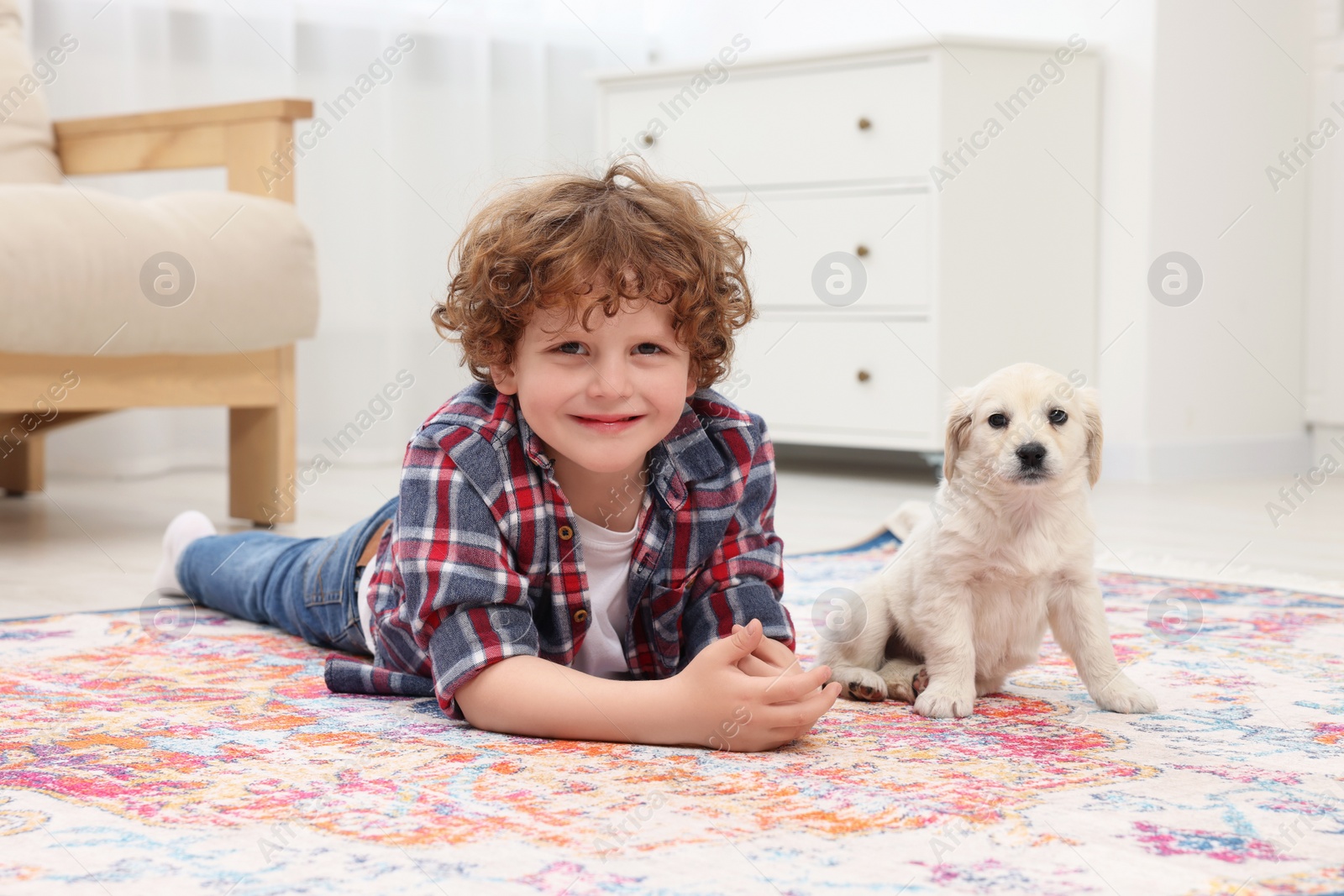 Photo of Little boy lying with cute puppy on carpet at home