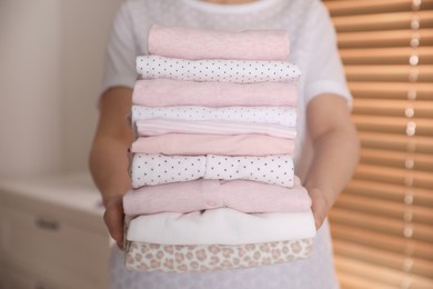 Photo of Woman holding stack of girl's clothes in bedroom, closeup