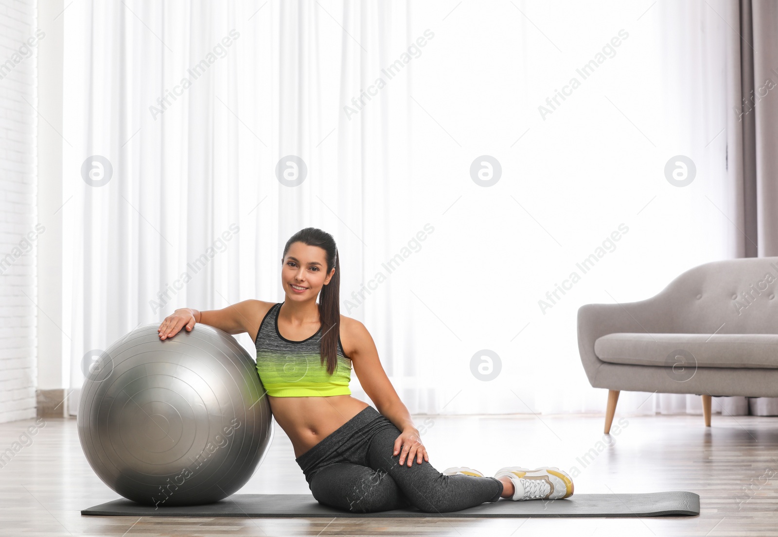 Photo of Young woman with fitness ball at home. Space for text