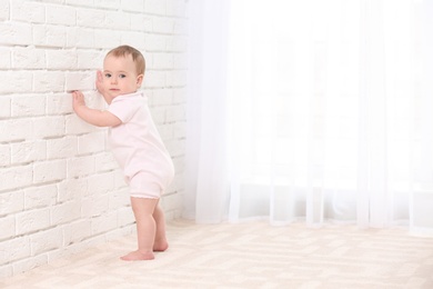Photo of Cute baby holding on to wall indoors. Learning to walk