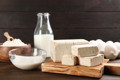 Pieces of compressed yeast near ingredients for dough on wooden table