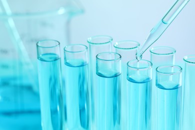 Dripping liquid from pipette into test tube on blurred background, closeup. Laboratory analysis