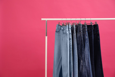 Photo of Rack with stylish jeans on pink background