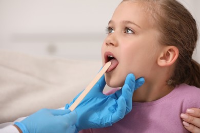 Doctor examining girl`s oral cavity with tongue depressor on blurred background, closeup. Space for text