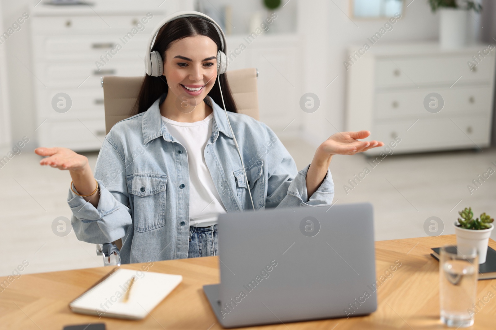 Photo of Young woman in headphones using video chat during webinar at table in room