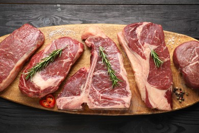 Photo of Pieces of raw beef meat and spices on black wooden table, top view