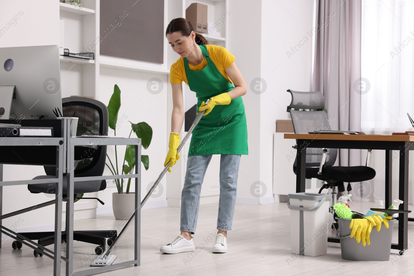 Photo of Cleaning service worker washing floor with mop. Bucket with supplies in office