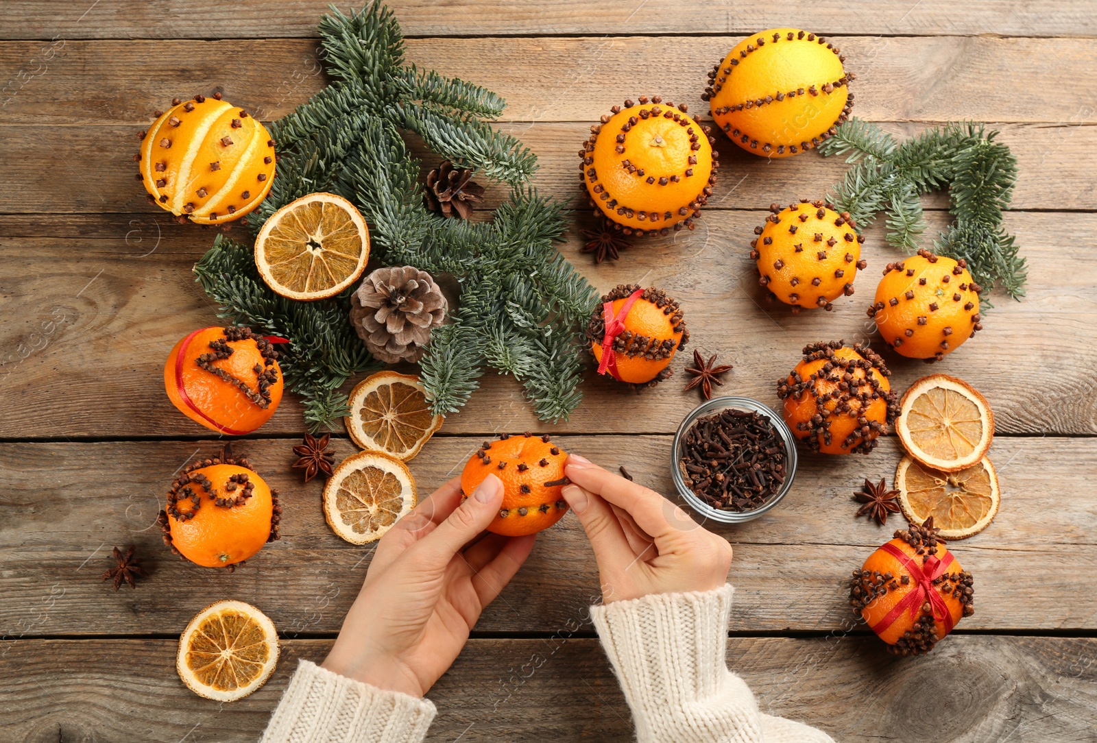 Photo of Woman decorating fresh tangerines with cloves at wooden table, top view. Making Christmas pomander balls