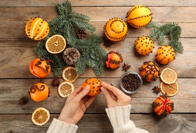 Photo of Woman decorating fresh tangerines with cloves at wooden table, top view. Making Christmas pomander balls