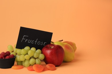 Photo of Card with word Fructose, delicious ripe fruits, raspberries and dried apricots on pale orange background. Space for text
