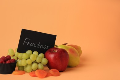 Card with word Fructose, delicious ripe fruits, raspberries and dried apricots on pale orange background. Space for text