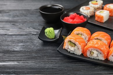 Photo of Tasty sushi rolls, wasabi, ginger and soy sauce on black wooden table