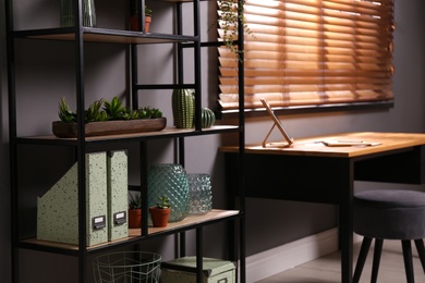 Photo of Shelving with different decor and houseplants near table in room. Interior design