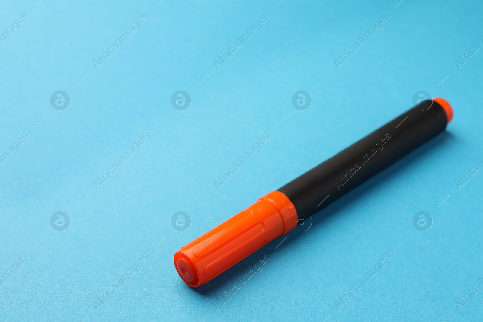 Photo of Bright orange marker on light blue background, space for text