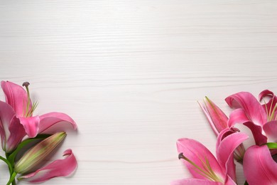 Beautiful pink lily flowers on white wooden table, flat lay. Space for text