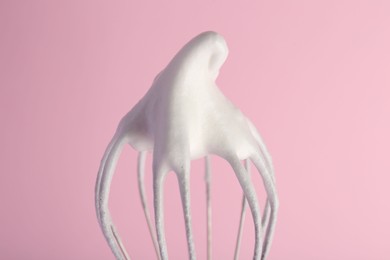 Photo of Whisk with whipped egg whites on pink background, closeup