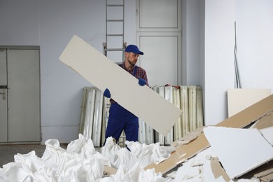 Photo of Construction worker carrying used drywall in room prepared for renovation