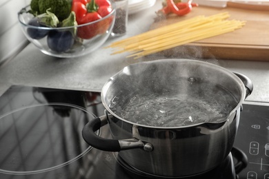 Pot with boiling water on electric stove in kitchen, space for text