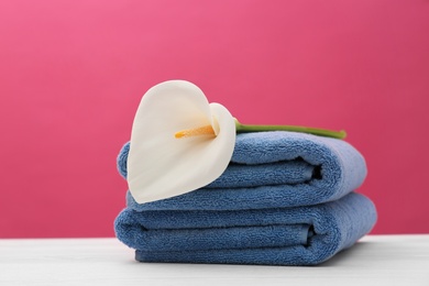 Soft clean towels with beautiful flower on table against color background