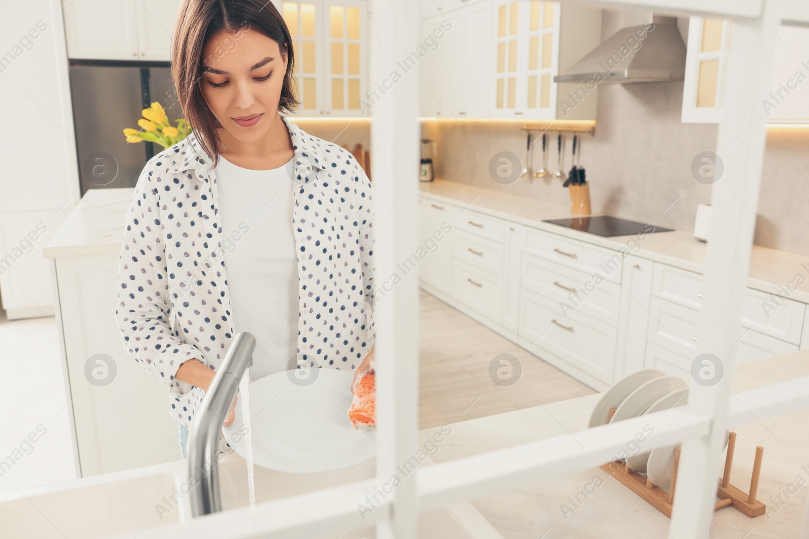 Photo of Happy young woman washing plate above sink in modern kitchen