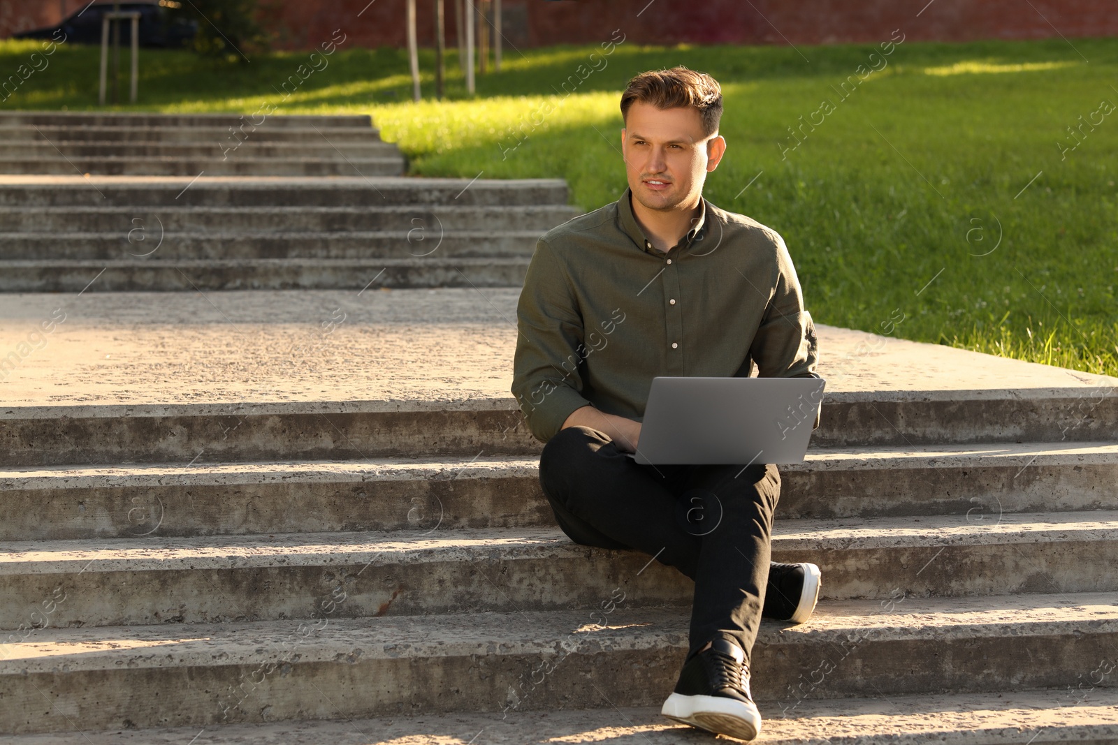 Photo of Handsome man with laptop sitting on concrete stairs outdoors. Space for text