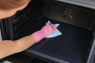 Photo of Woman cleaning oven with rag in kitchen, closeup