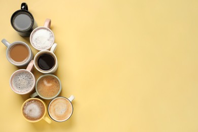 Many different cups with aromatic coffee on yellow table, flat lay. Space for text