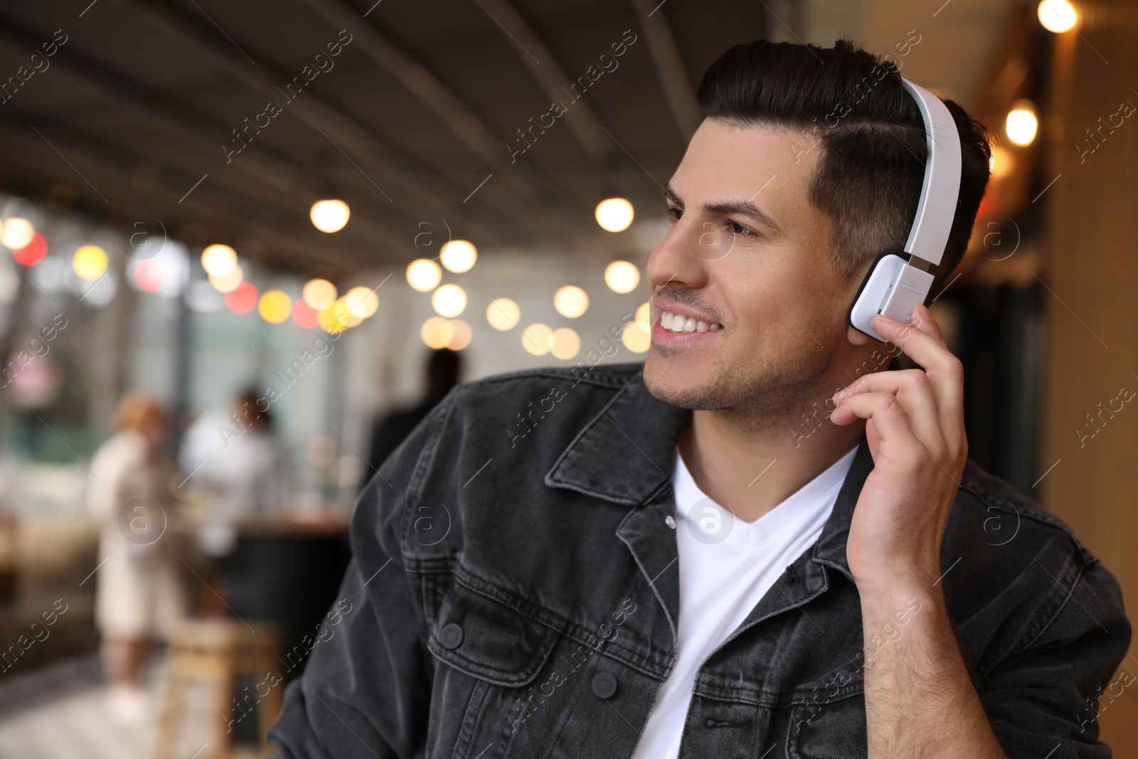 Photo of Handsome man with headphones listening to music in outdoor cafe, space for text