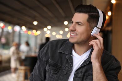 Handsome man with headphones listening to music in outdoor cafe, space for text