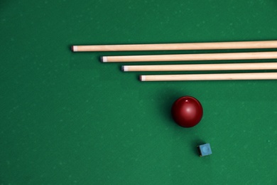 Red billiard ball, chalk and cues on table, flat lay. Space for text